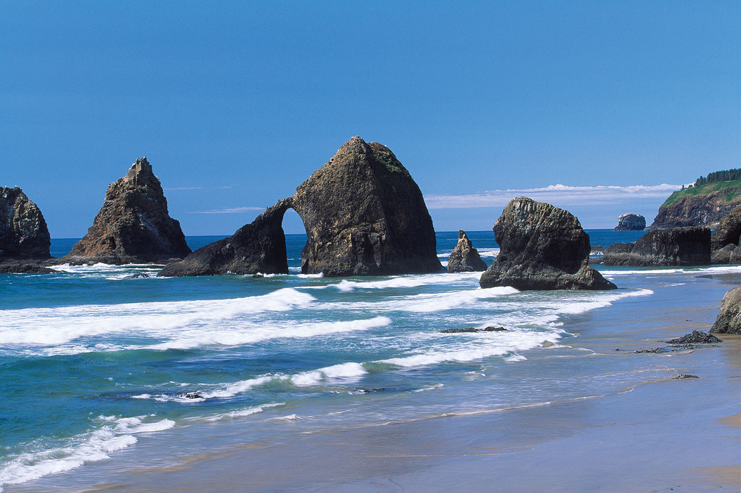 Jagged rock formations emerge from the Pacific Ocean and form a natural arch near Oceanside, Oregon.