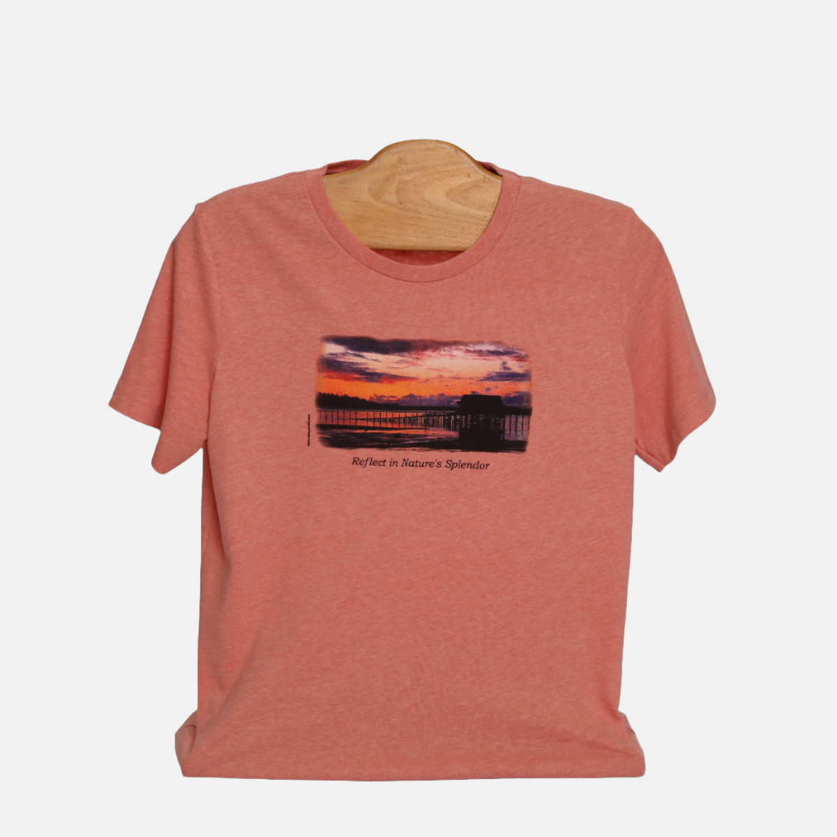 Front view of Sunset Beach short sleeve T-shirt, colored pink. Features print of sunset on coastal waters of Garabaldi, Oregon. Caption below reads "Reflect in Nature's Splendor".