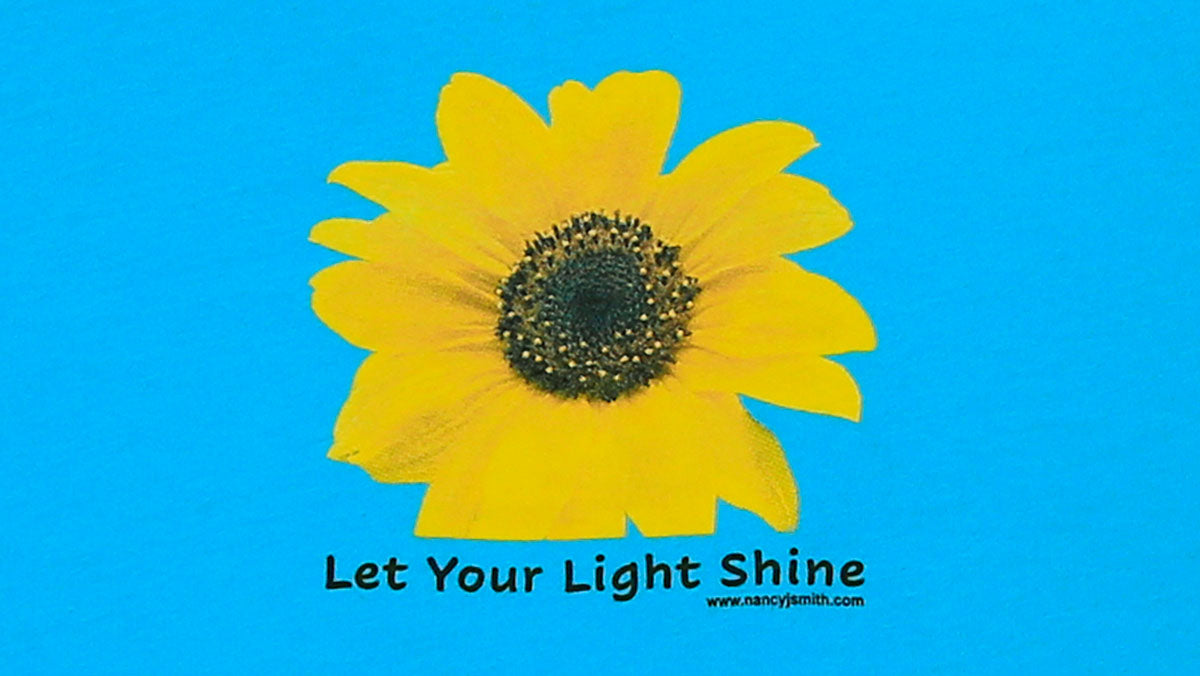 Detail view of shirt screen print. Sunflower with caption "Let Your Light Shine".
