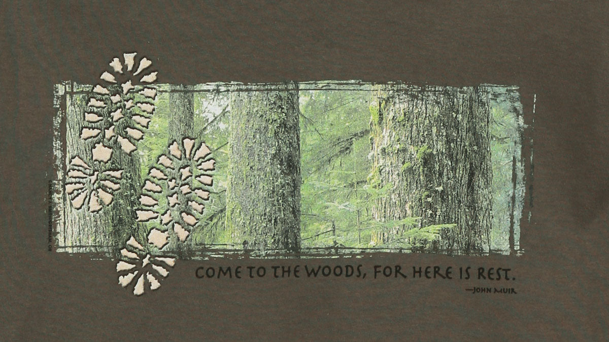 Detail view of shirt screen print. Features trees and two footprints, captioned "come to the woods, for here is rest".