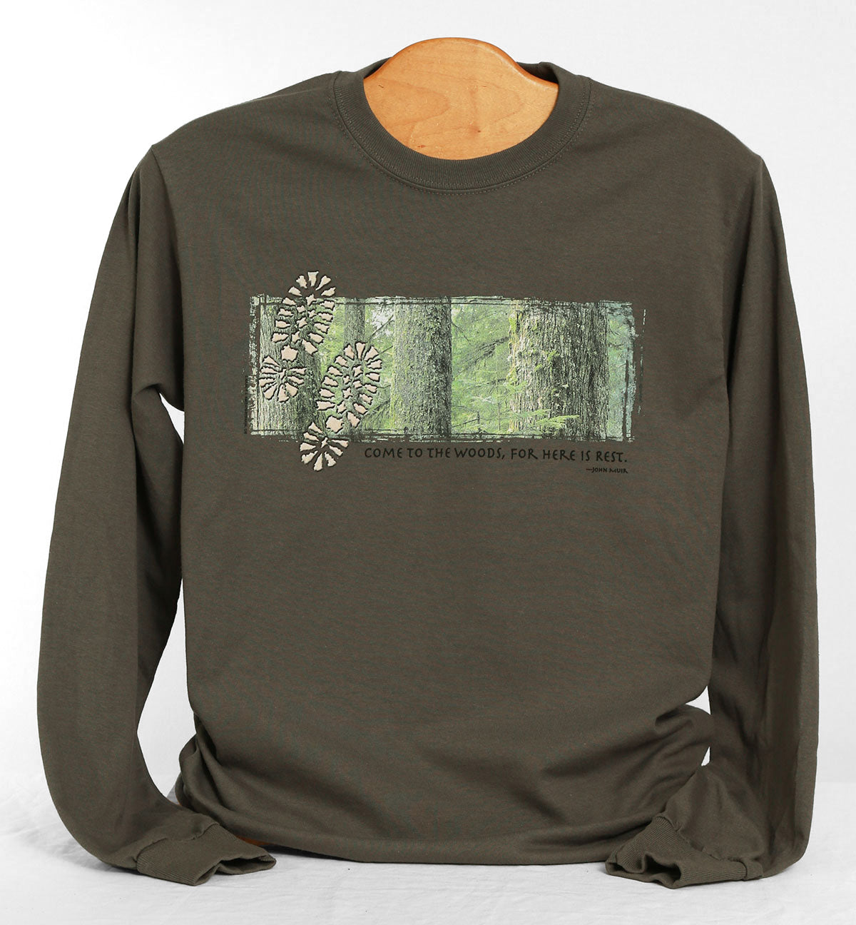 Front view of Come to The Woods long sleeve shirt, color charcoal. Features print of detail view of trees, with two footprints. Caption reads "Come to the woods, for here is rest".