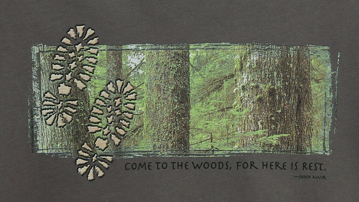 Detail view of shirt print on asphalt grey. Features tree trunks against forest background with two footprints and caption "Come to the woods, for here is rest."