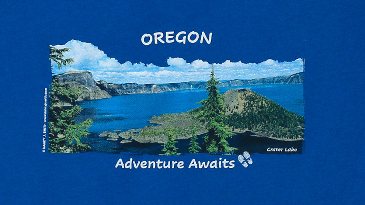 Detail view of shirt screen print on royal blue, featuring Wizard Island in Crater Lake National Park, Oregon, with caption "Adventure Awaits".