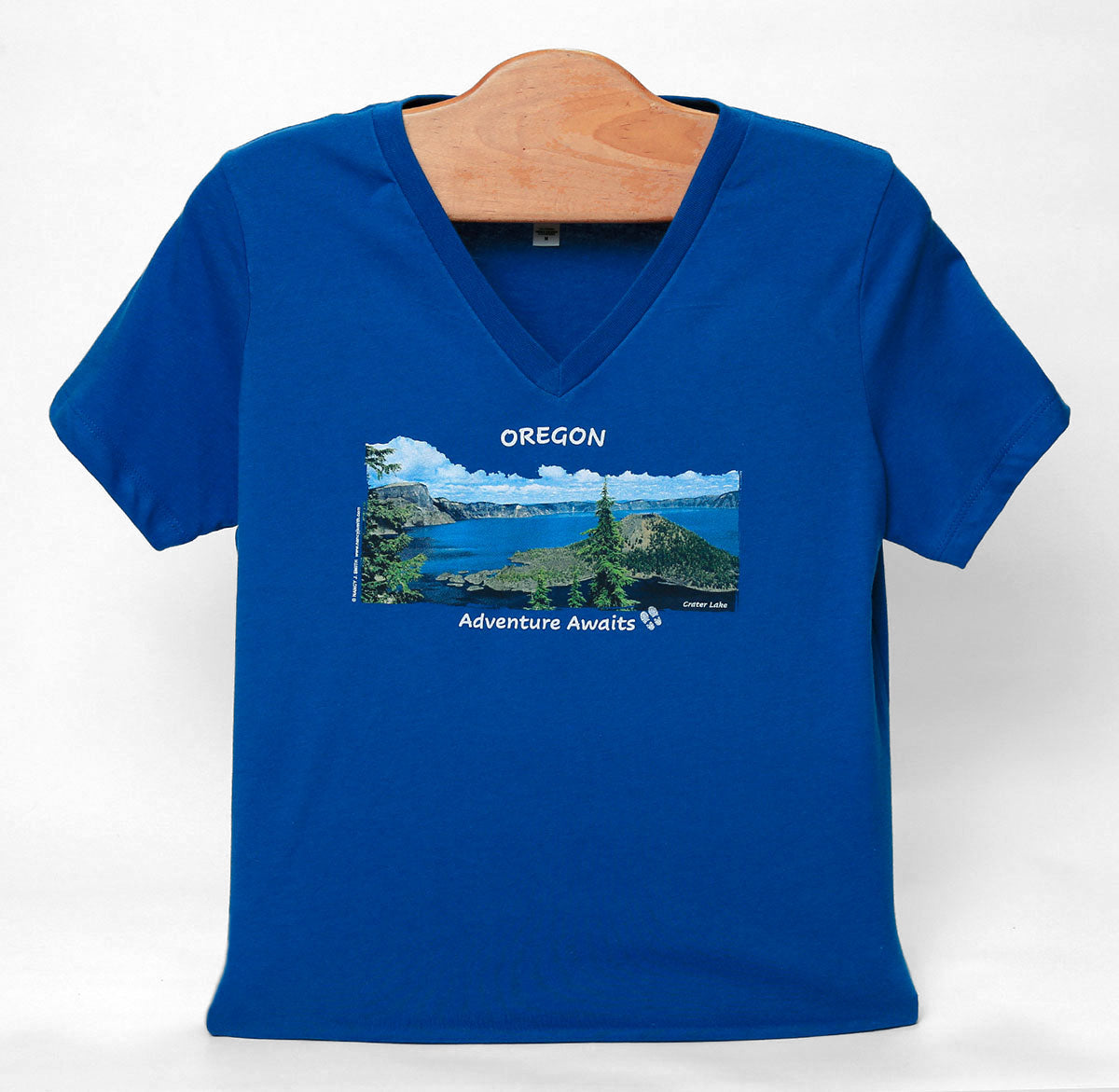 Front view of Crater Lake v-neck t-shirt in color royal blue. Features screen print of Wizard Island in Crater Lake National Park, Oregon with caption "Adventure Awaits".