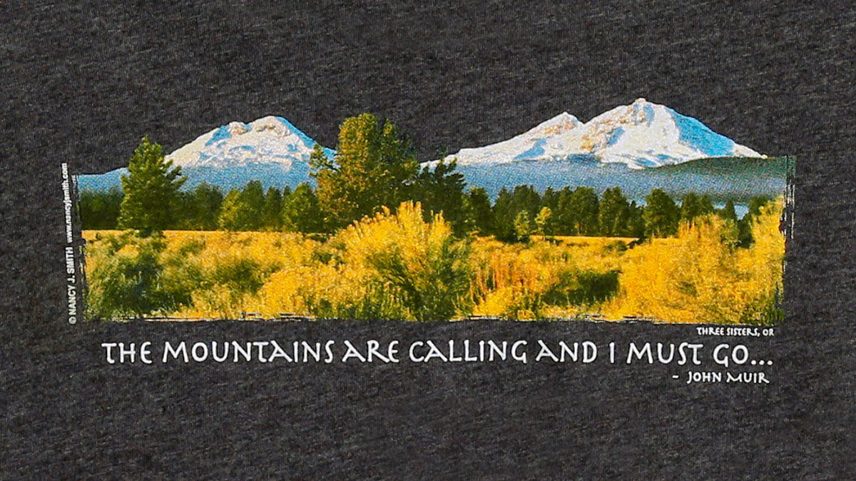 Detail view of shirt screen print on dark heather grey, featuring Oregon's Three Sisters mountains and caption "The Mountains are Calling and I Must Go...".