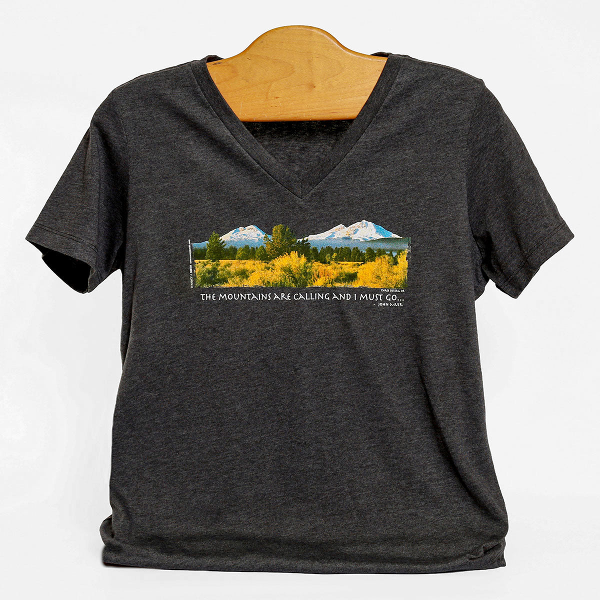Front view of Three Sisters/Mountains are Calling v-neck t-shirt in dark heather grey. Print features Oregon's Three Sisters mountains and caption "The Mountains are Calling and I Must Go...".