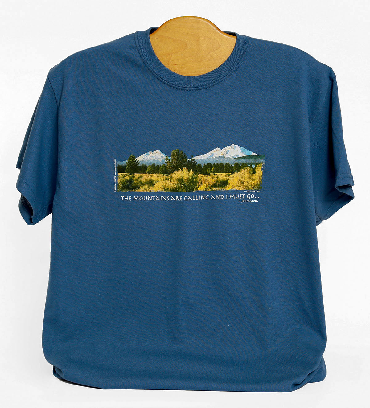 Front view of Three Sisters/Mountains are Calling t-shirt in color indigo blue. Features screen print of Oregon's Three Sisters mountains and caption "The Mountains are Calling and I Must Go...".