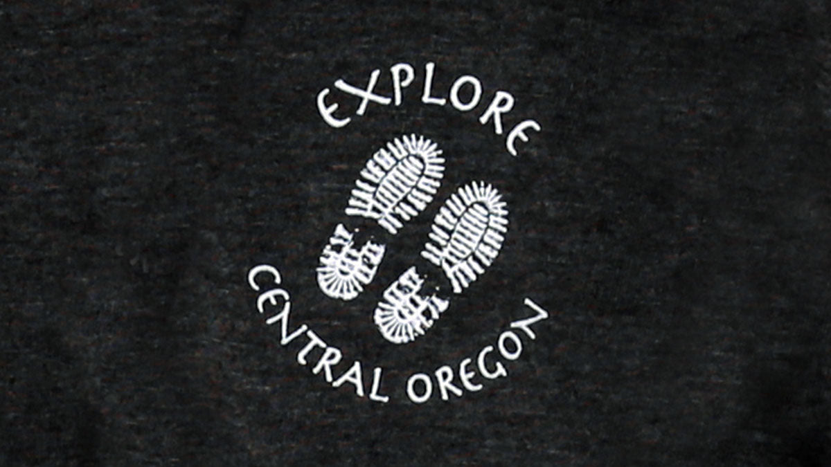 Detail view of hoodie screen print featuring two footprints and text "Explore Central Oregon".