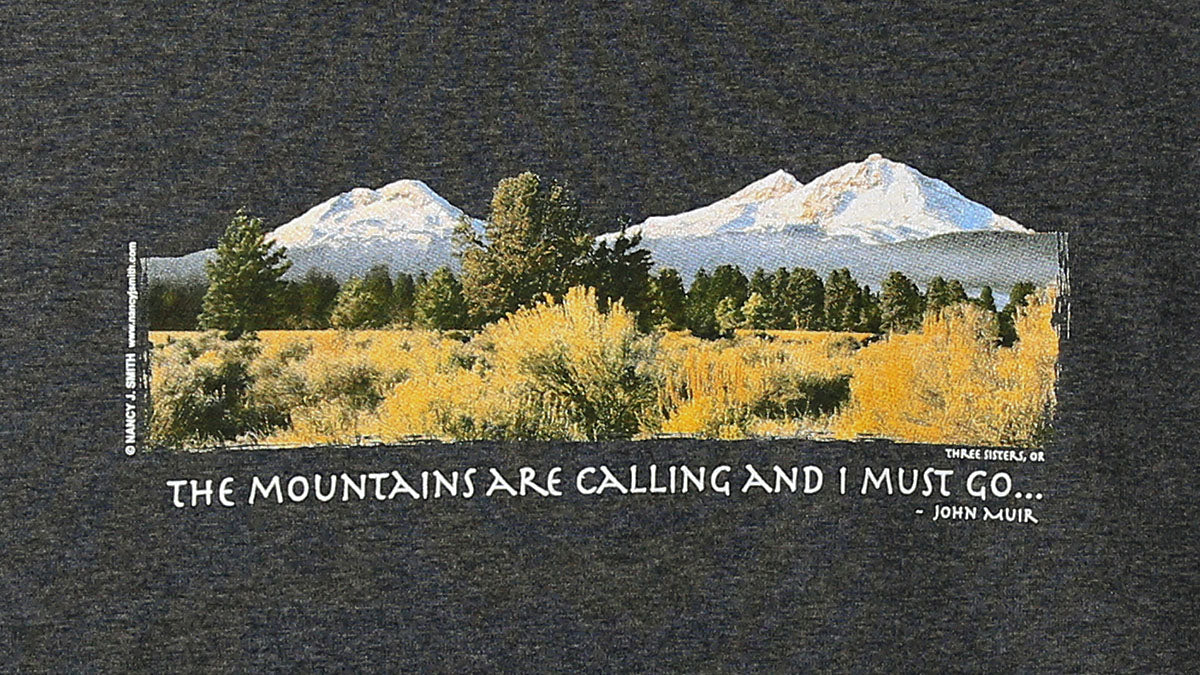 Detail view of shirt screen print, featuring Oregon's Three Sisters mountains and caption "The Mountains are Calling and I Must Go...".