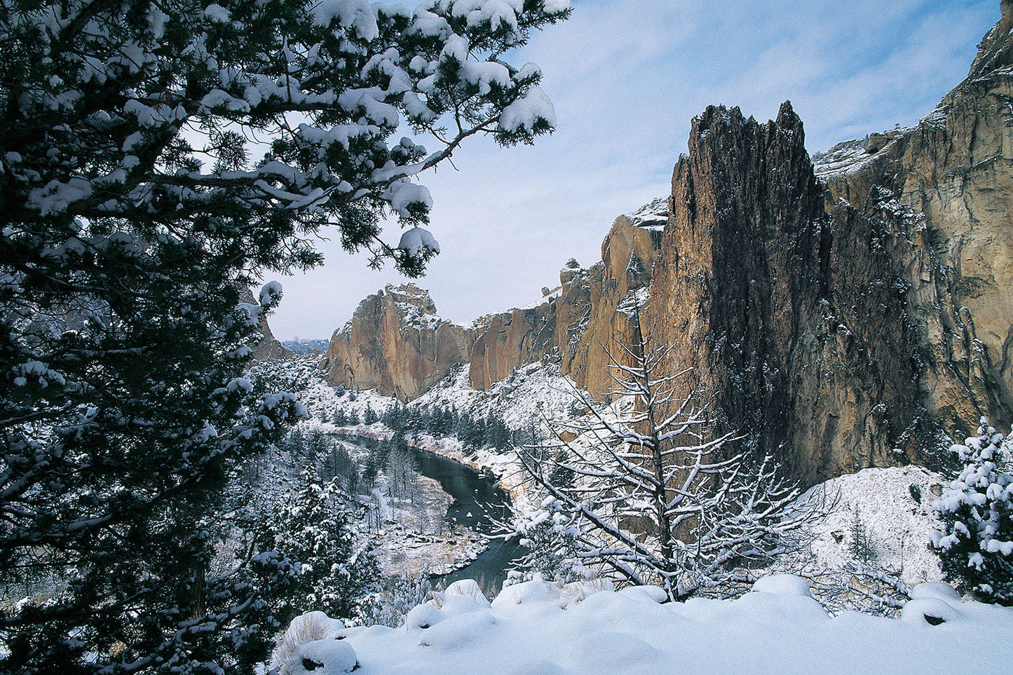 Snow covers the ground and dusts rocky cliffs in Smith Rock State Park, Oregon. The Crooked River winds through the Winter scene.